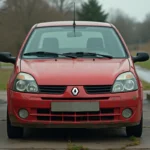 Renault Clio 2 rouge garée à une station-service rurale avec jauge de carburant presque vide visible sur le tableau de bord