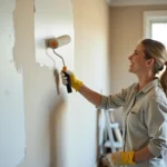 Femme en train de peindre un mur intérieur en blanc lors de travaux de rénovation maison